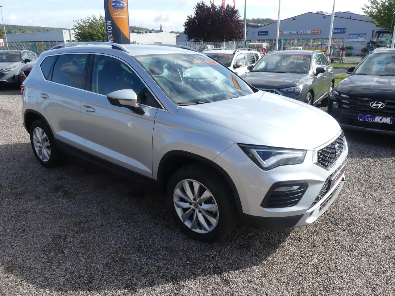 SEAT Ateca gris clair vue 3/4 avant droit, avec jantes alliage 17'' et calandre chromée sur parking extérieur.