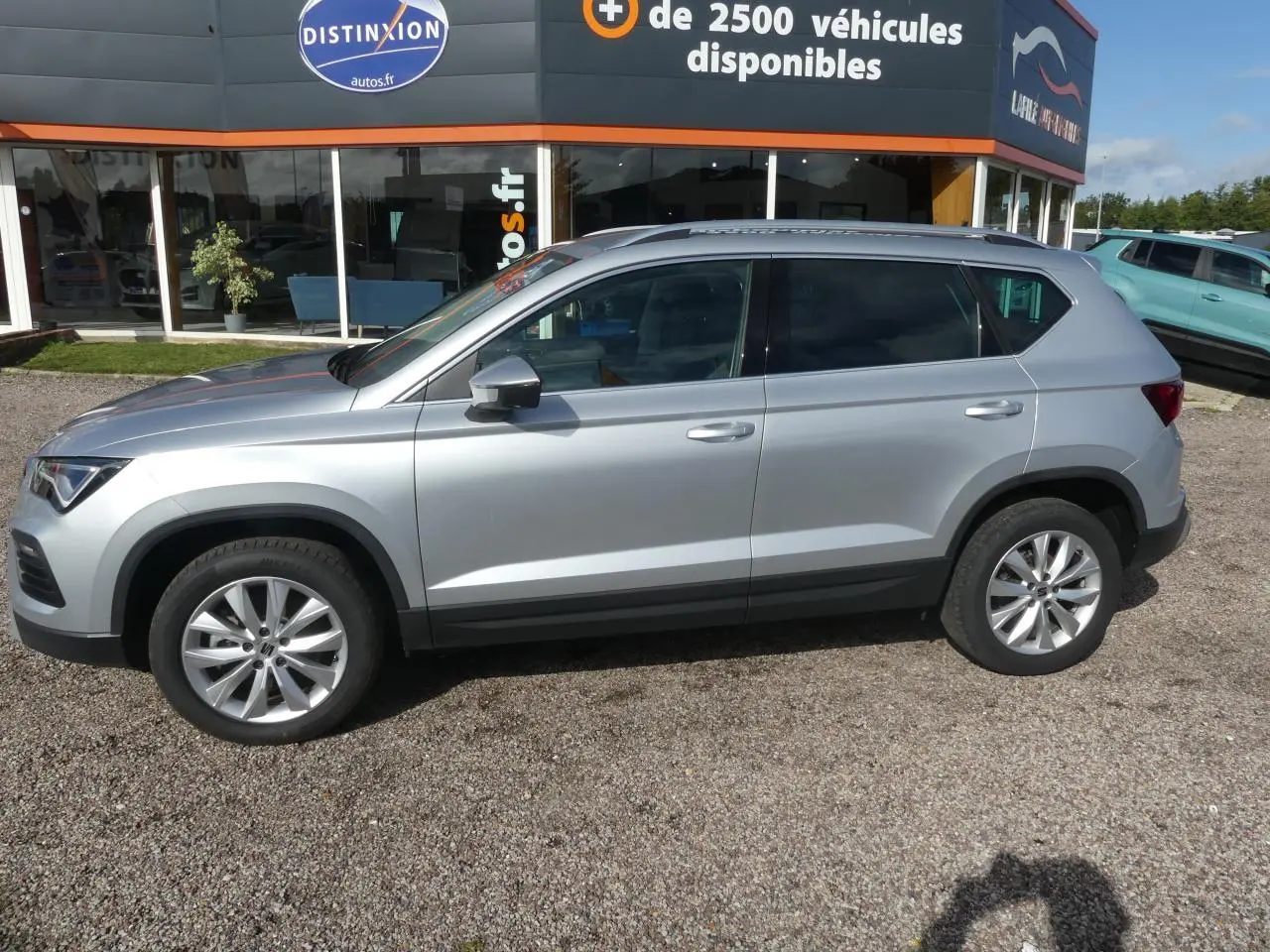 Vue de profil côté gauche d'un SUV SEAT Ateca gris clair garé devant un concessionnaire avec jantes alliage 17 pouces.