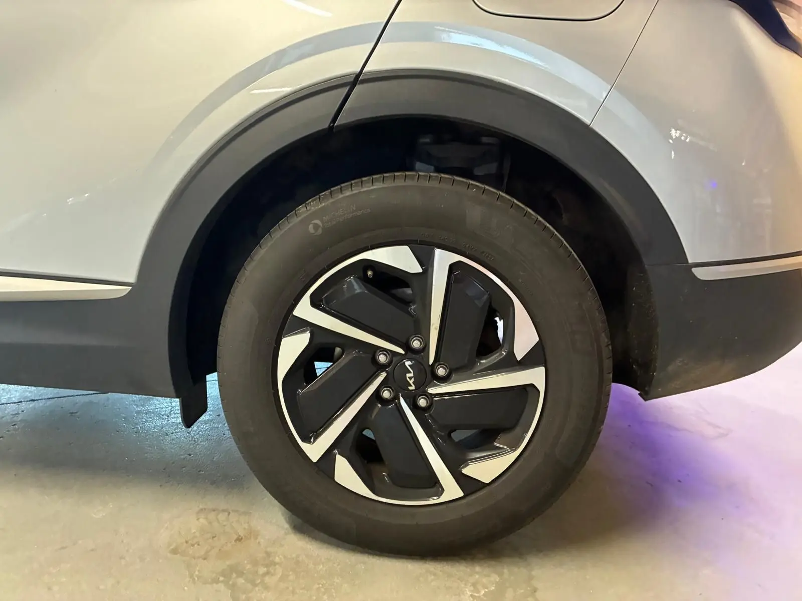 Gros plan sur la roue arrière droite du KIA Sportage gris 2024, mettant en valeur la jante noire et argentée au design moderne.