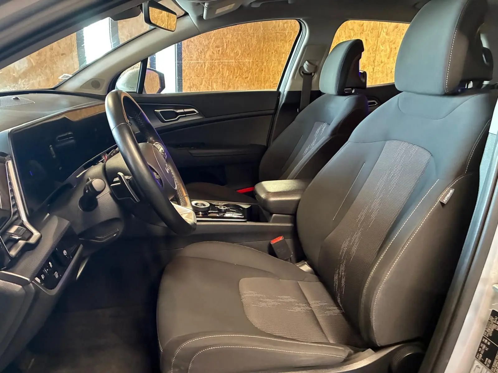 Vue intérieure côté conducteur du Kia Sportage 2024 gris, montrant sièges noirs et tableau de bord moderne avec écran tactile.