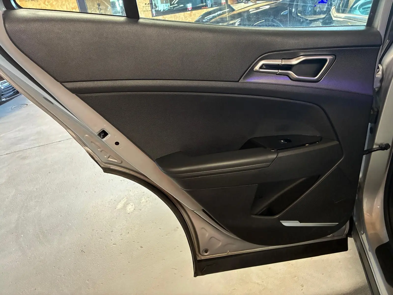 Vue intérieure de la porte arrière droite du Kia Sportage gris 2024, avec garniture noire et poignée argentée.