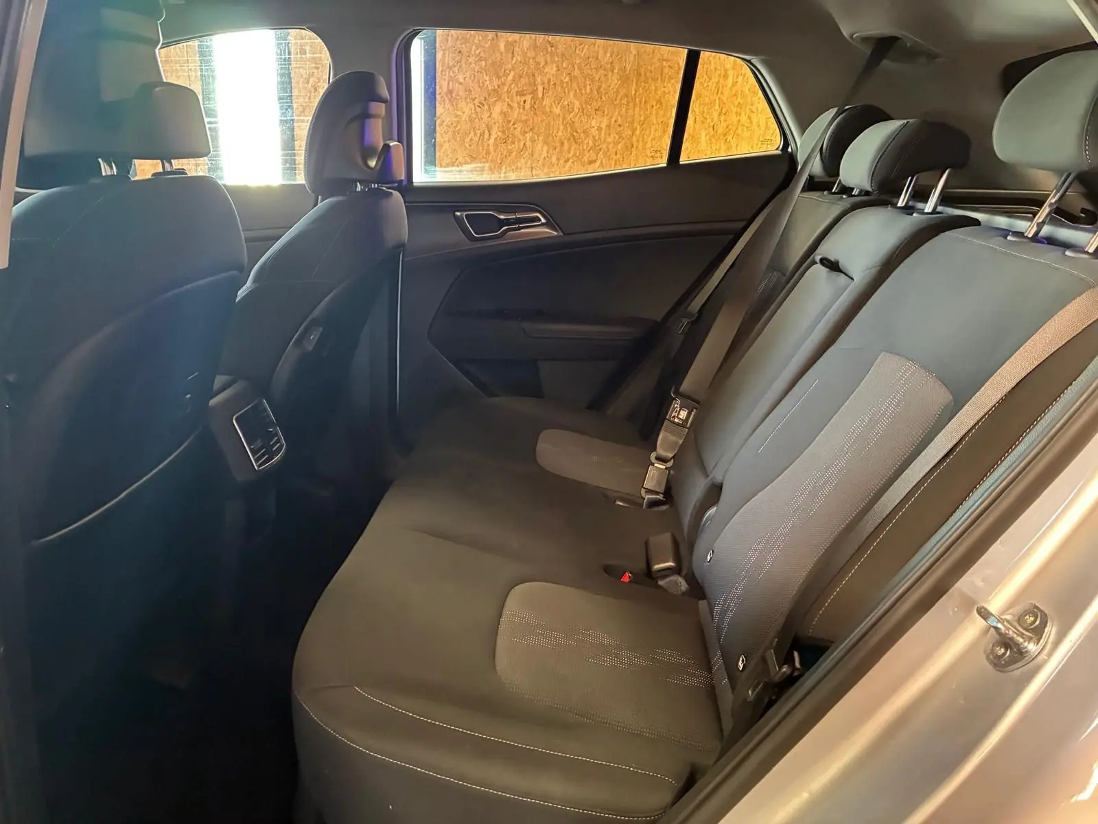 Vue intérieure côté droit sur les sièges arrière noirs du Kia Sportage hybride gris 2024, avec ceinture de sécurité visible.
