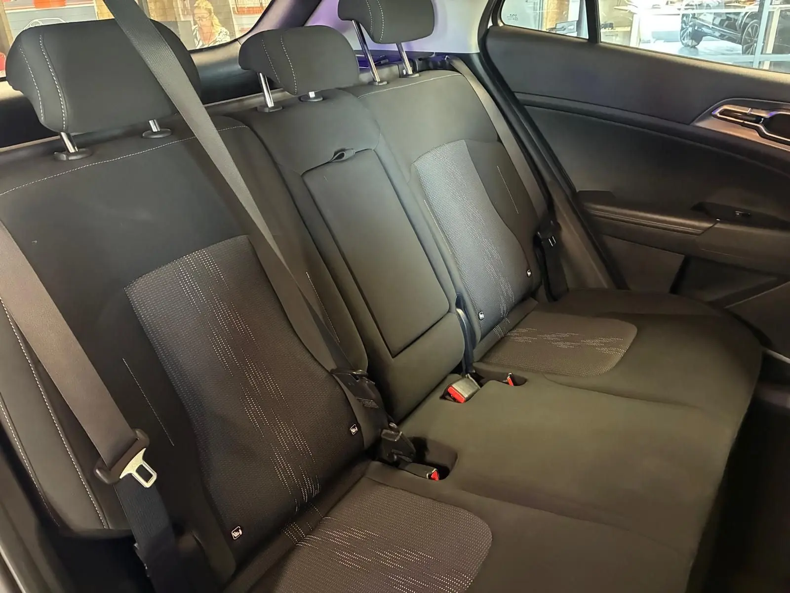Vue intérieure des sièges arrière en tissu noir du Kia Sportage hybride 2024, avec ceinture de sécurité et accoudoir central rabattable.