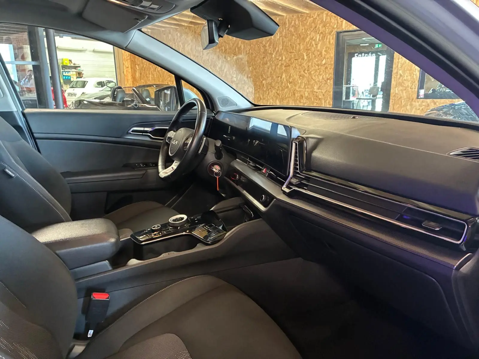 Vue intérieure côté conducteur du Kia Sportage hybride 2024, avec tableau de bord moderne et sellerie noire.