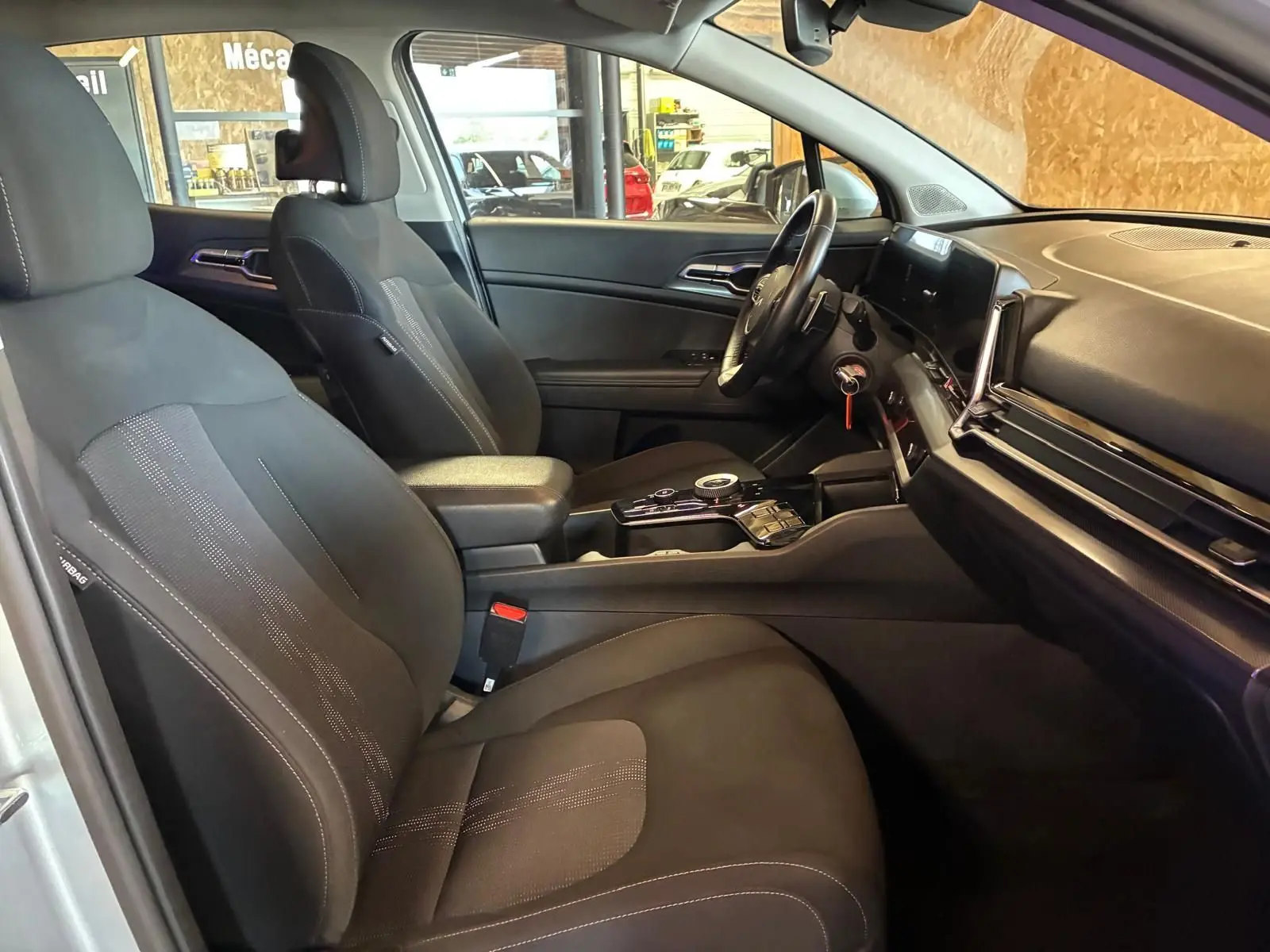 Vue intérieure côté conducteur du Kia Sportage 2024 gris, montrant sièges noirs et tableau de bord moderne avec écran tactile.