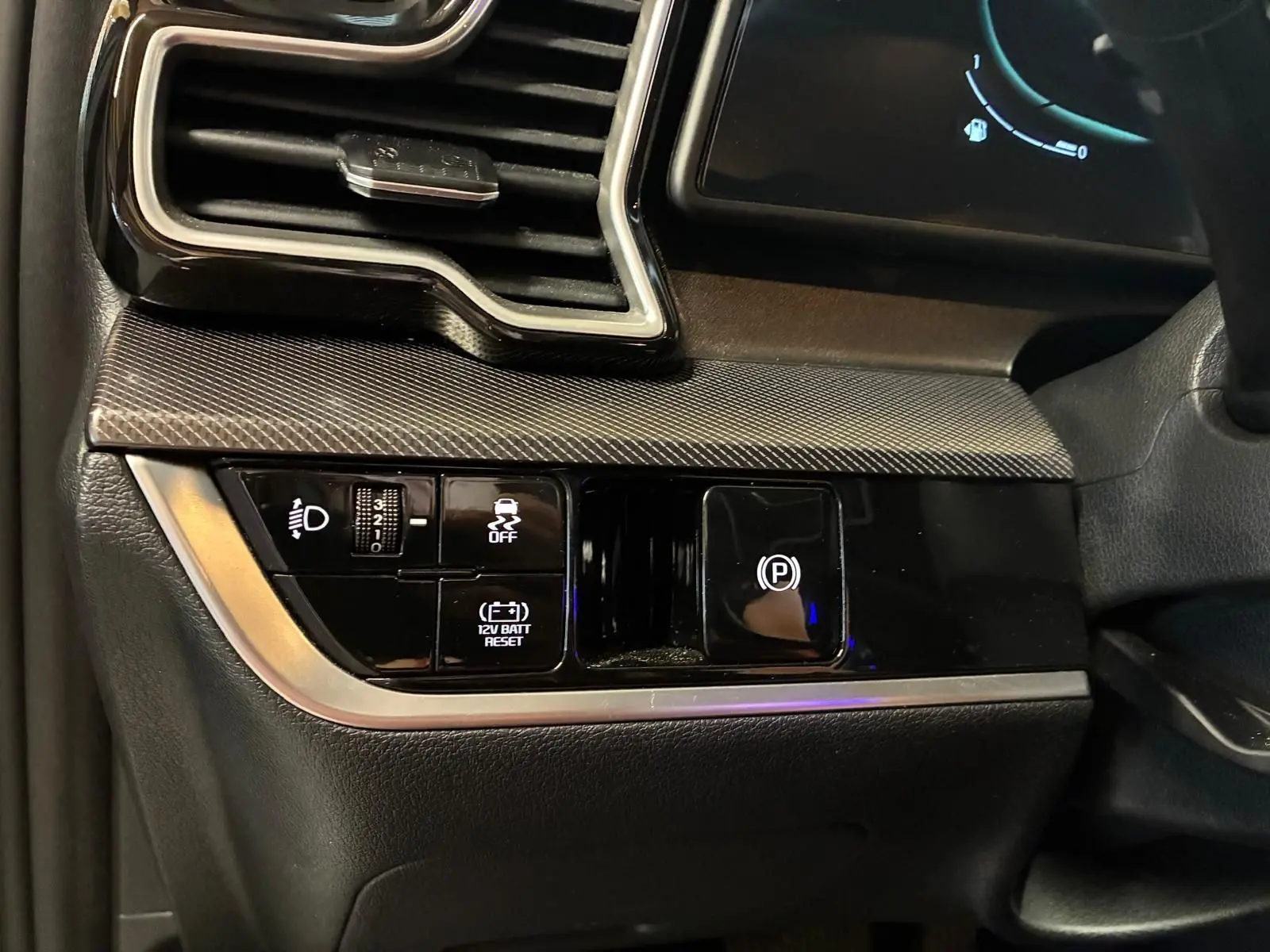 Détail du tableau de bord côté gauche du Kia Sportage gris 2024, avec commandes d'éclairage et frein à main électronique.
