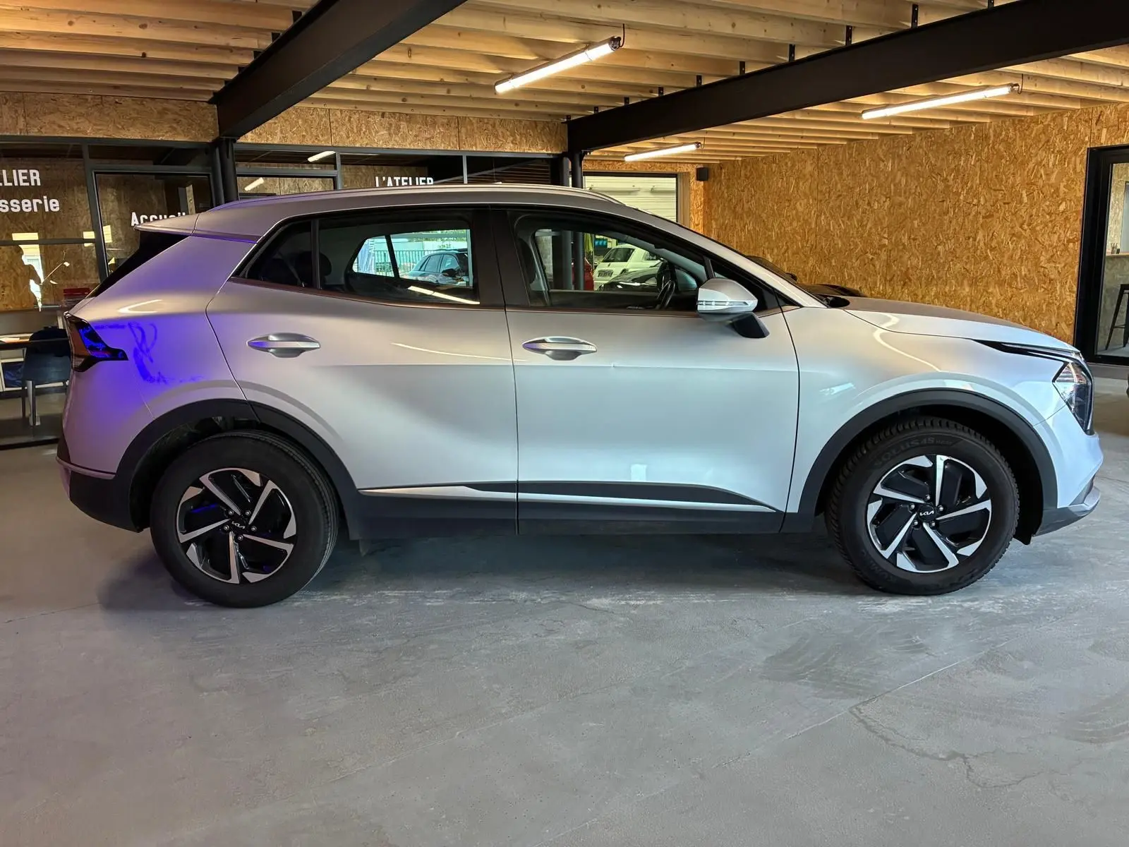 Vue de profil côté gauche d'un KIA Sportage 2024 gris hybride avec jantes noires et détails modernes.