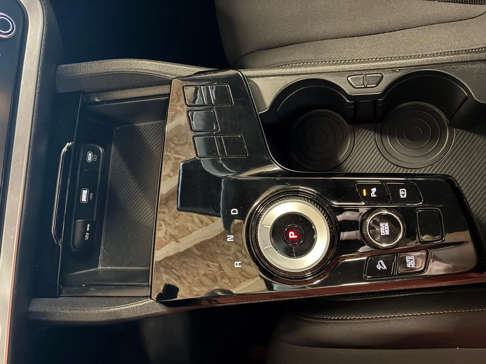Vue rapprochée de la console centrale noire brillante du Kia Sportage 2024 hybride avec molette de sélection de vitesse et porte-gobelets.
