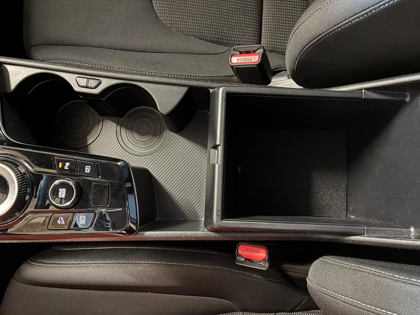 Vue plongeante sur la console centrale du Kia Sportage hybride 2024, avec rangement ouvert et commandes de boîte auto.