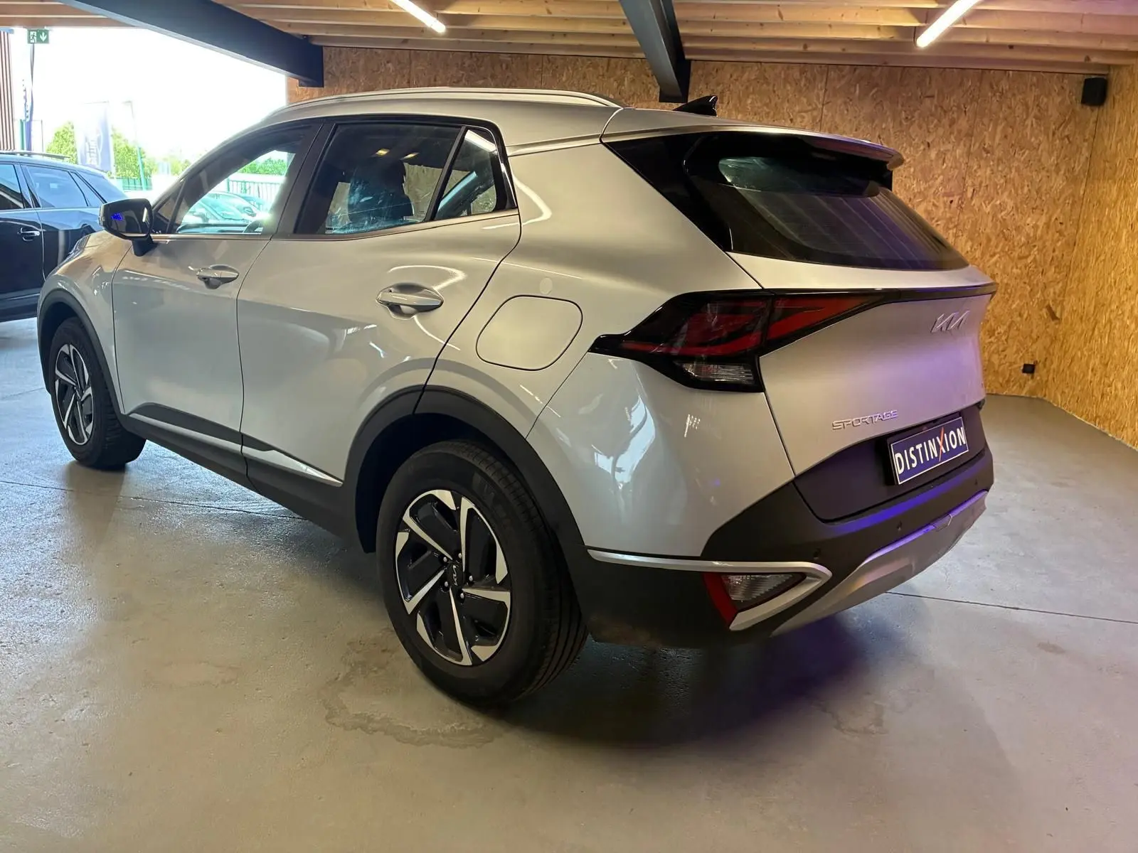 Vue 3/4 arrière droite du KIA Sportage gris 2024 hybride, avec feux arrière distinctifs et jantes bicolores.