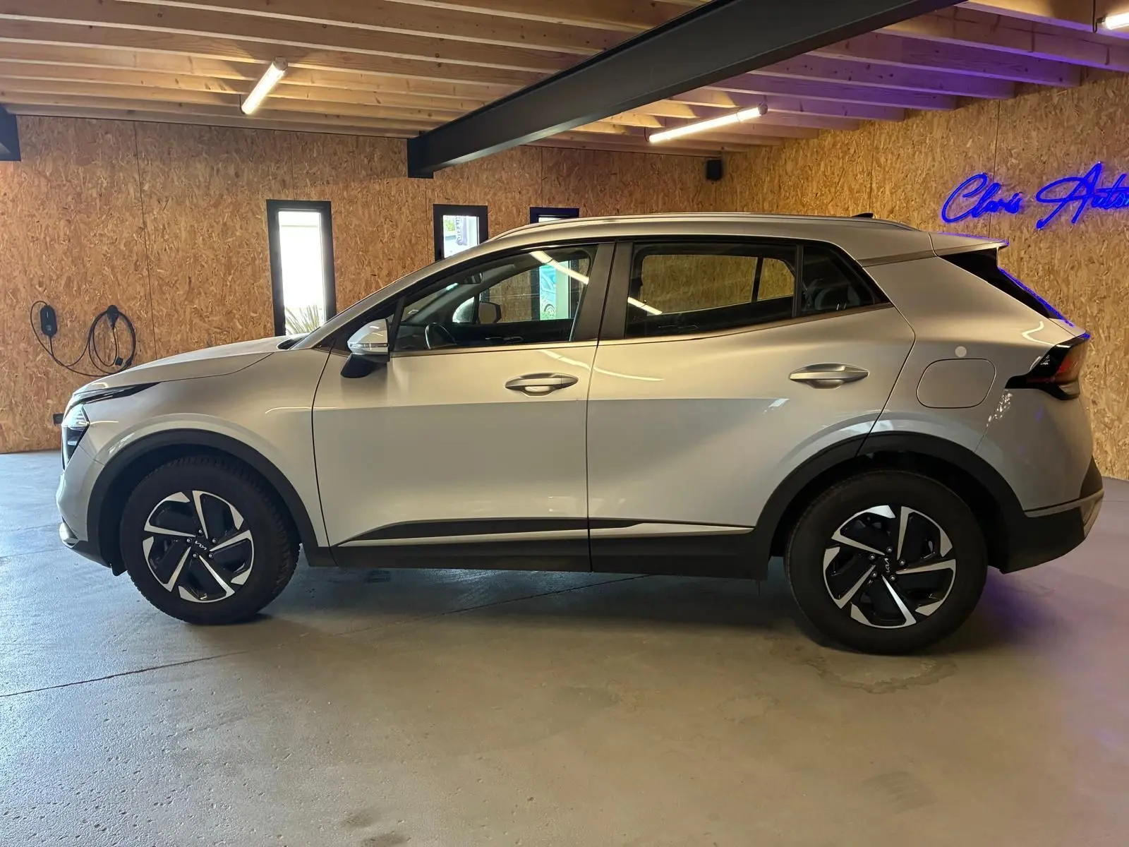 Vue de profil côté gauche du KIA Sportage 2024 gris hybride, avec jantes noires et détails noirs contrastants.