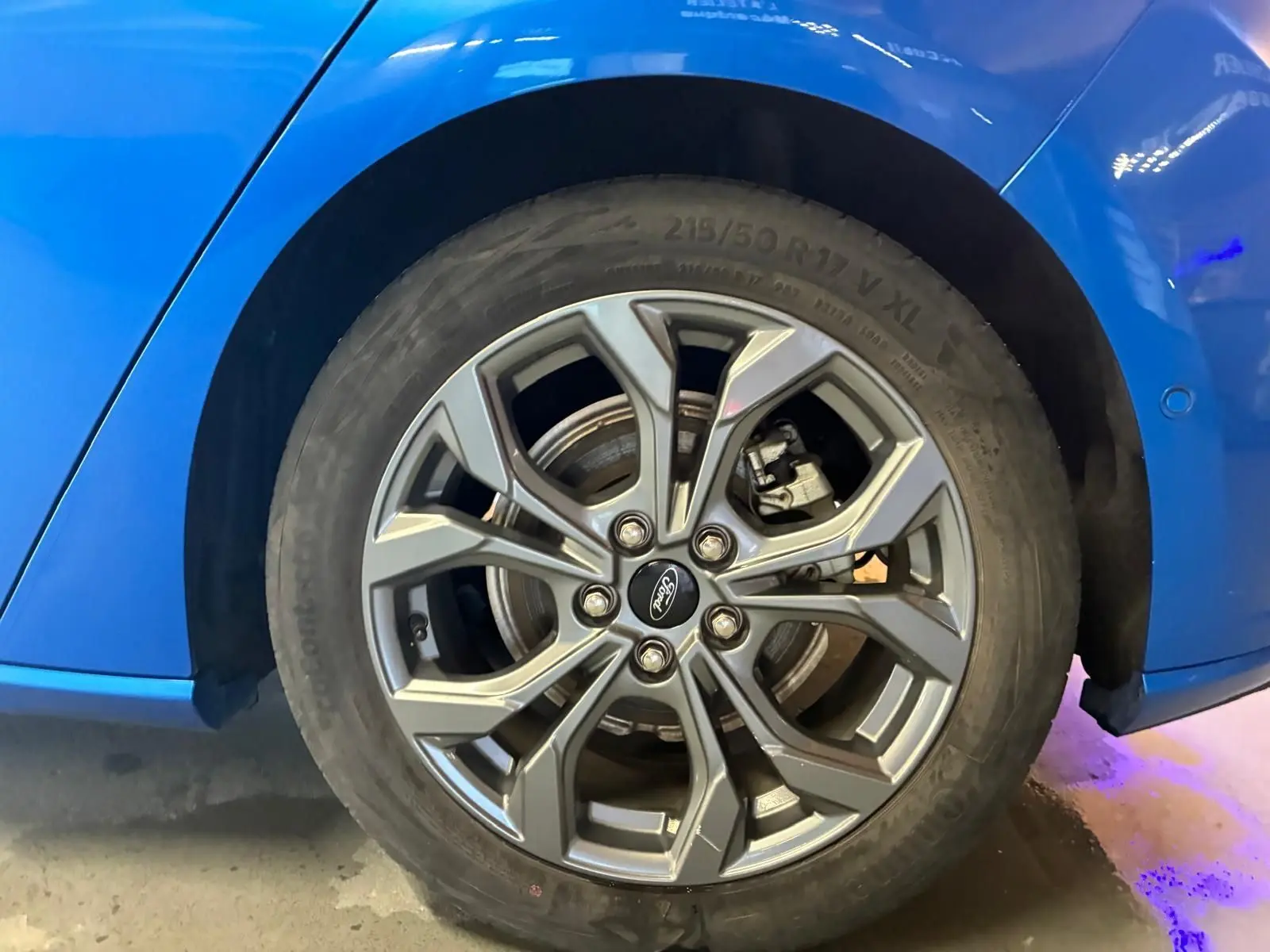 Gros plan sur la roue arrière droite d'une Ford Focus bleue 2024, mettant en valeur la jante alliage au design moderne.