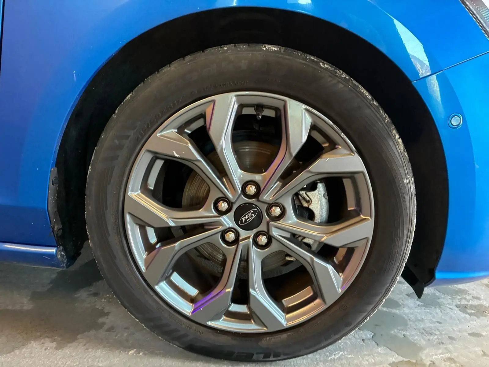 Gros plan sur la roue avant droite d'une Ford Focus bleu 2024, mettant en valeur la jante alliage au design moderne.
