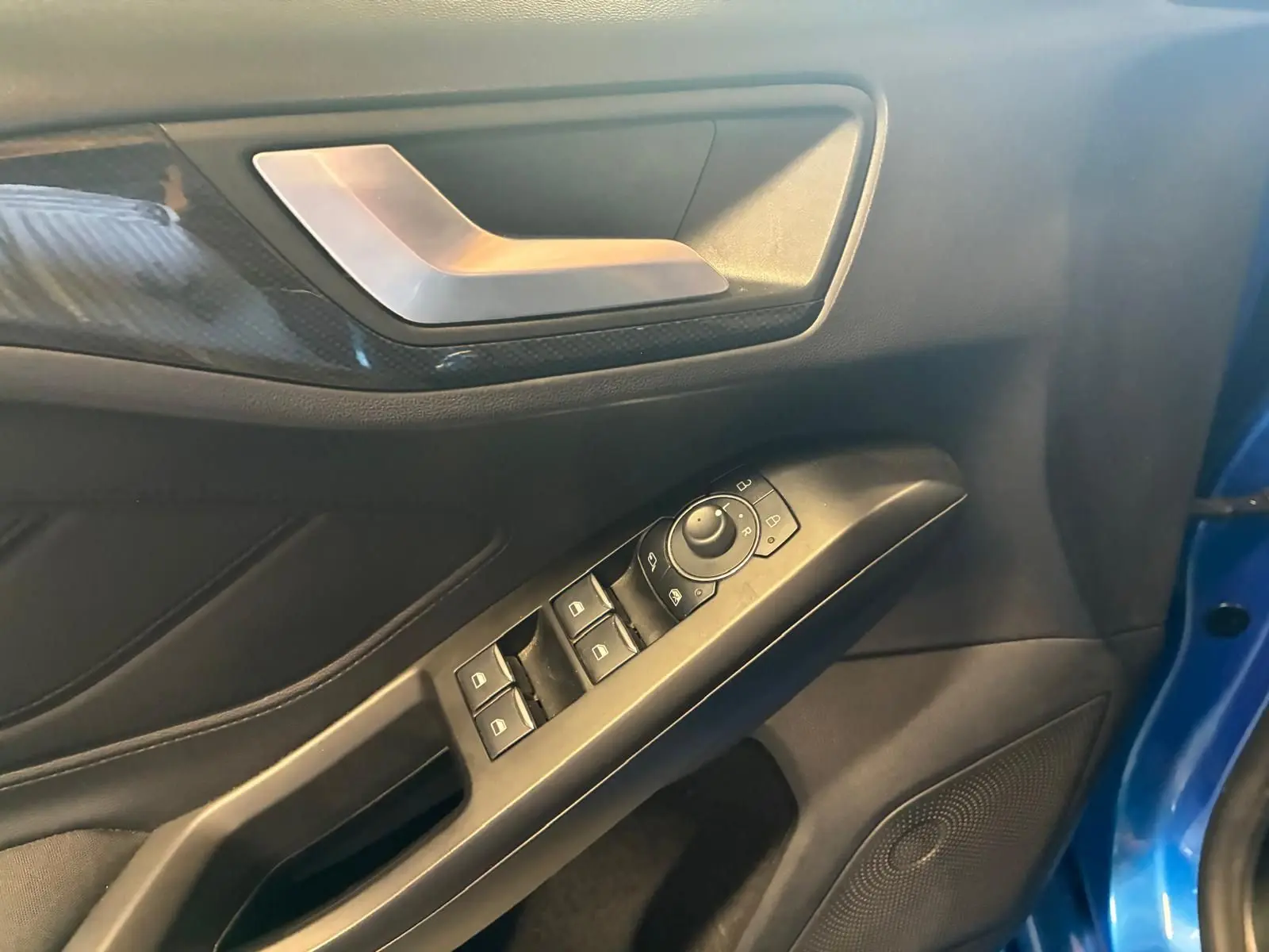 Détail de la porte avant gauche de la Ford Focus bleue 2024, avec commandes électriques des vitres et poignée argentée.