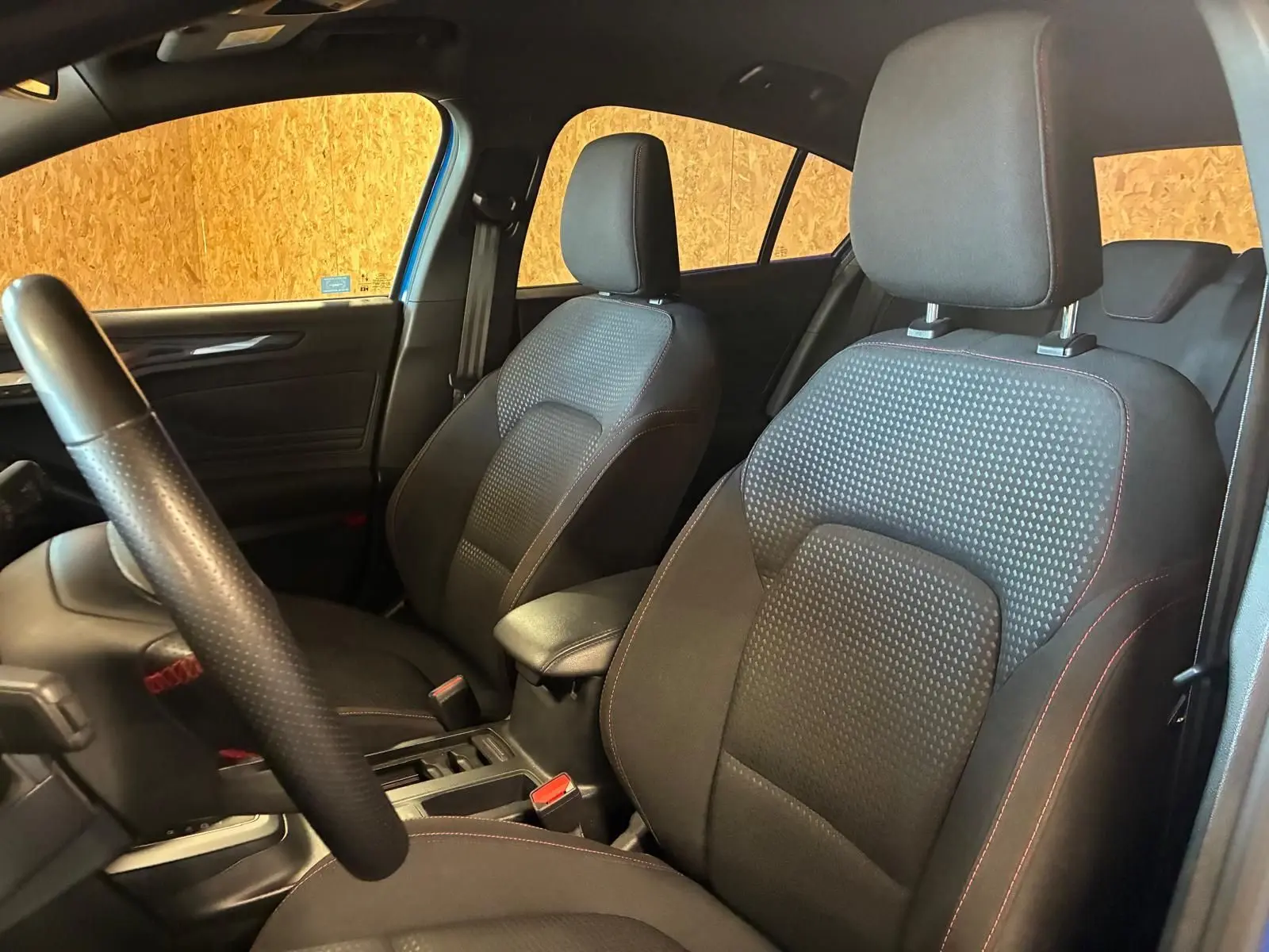Vue intérieure côté gauche de la Ford Focus 2024 bleu, sièges avant en tissu noir avec surpiqûres rouges.