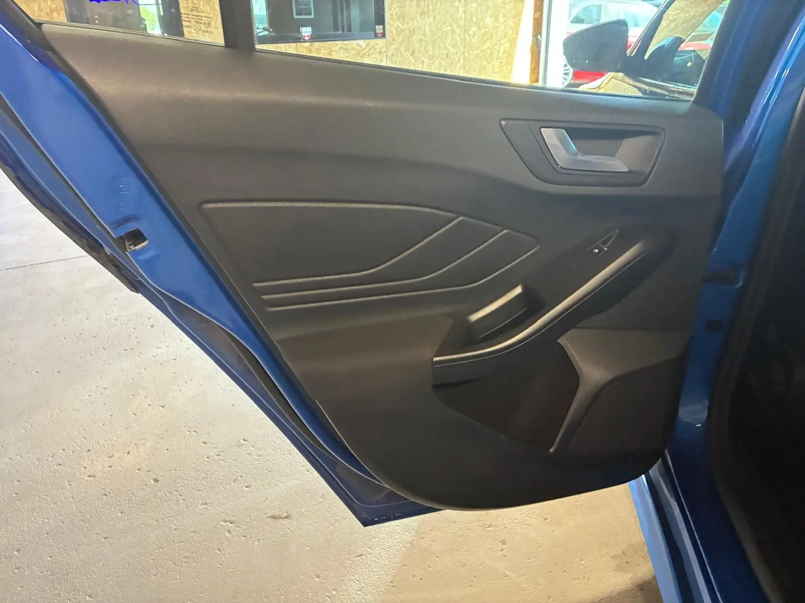 Vue rapprochée de la porte arrière gauche bleue d'une Ford Focus 2024, avec garniture intérieure noire et poignée intégrée.
