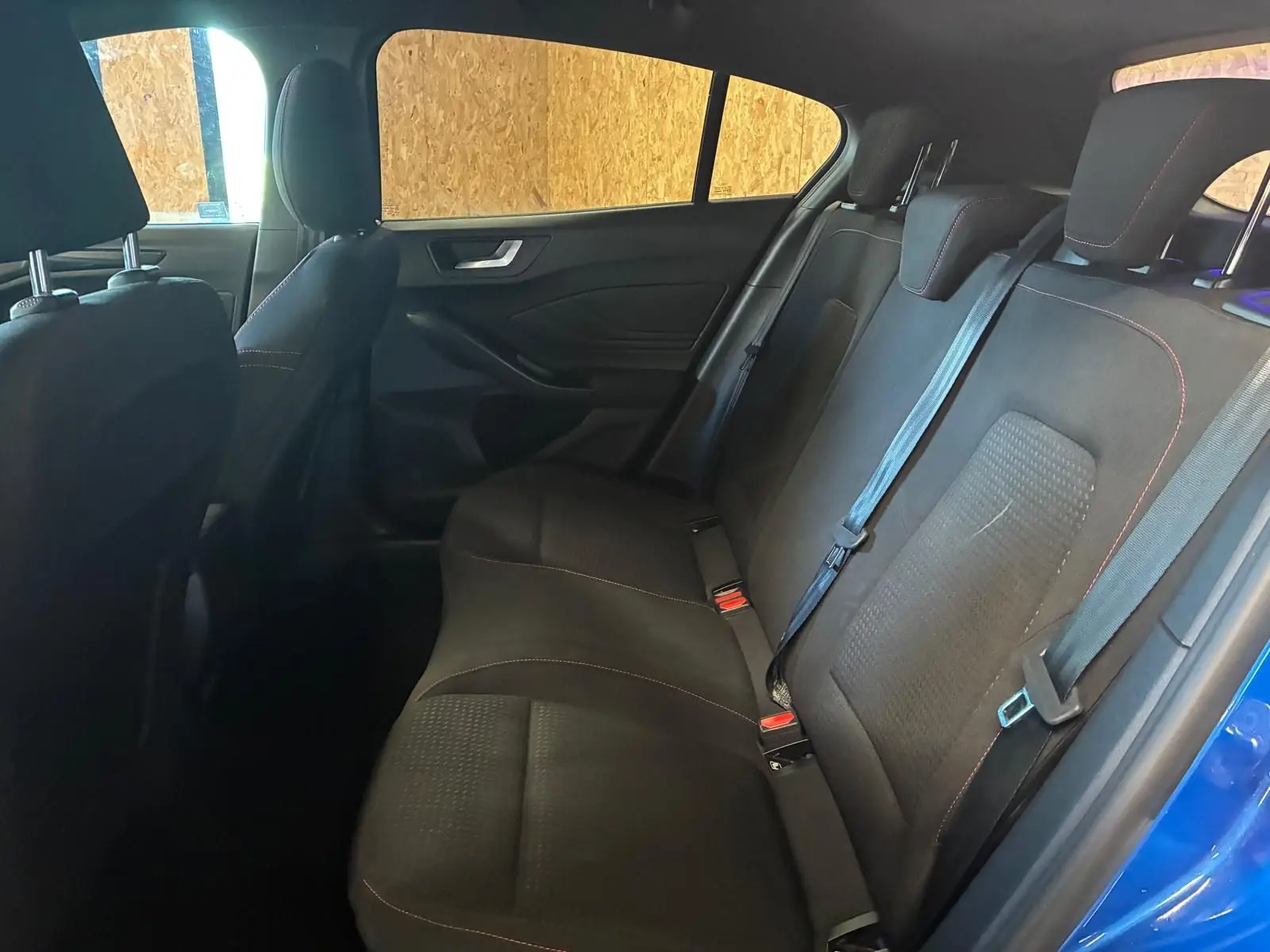 Vue intérieure arrière côté droit de la Ford Focus 2024 bleu, montrant les sièges arrière en tissu noir avec surpiqûres rouges.