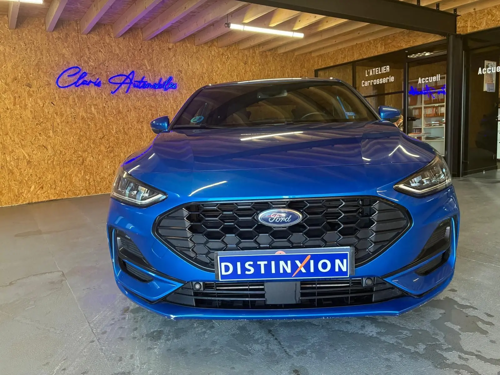 Vue frontale d'une Ford Focus 1.0 EcoBoost MHEV bleu vif, avec calandre hexagonale noire et logo Ford centré.