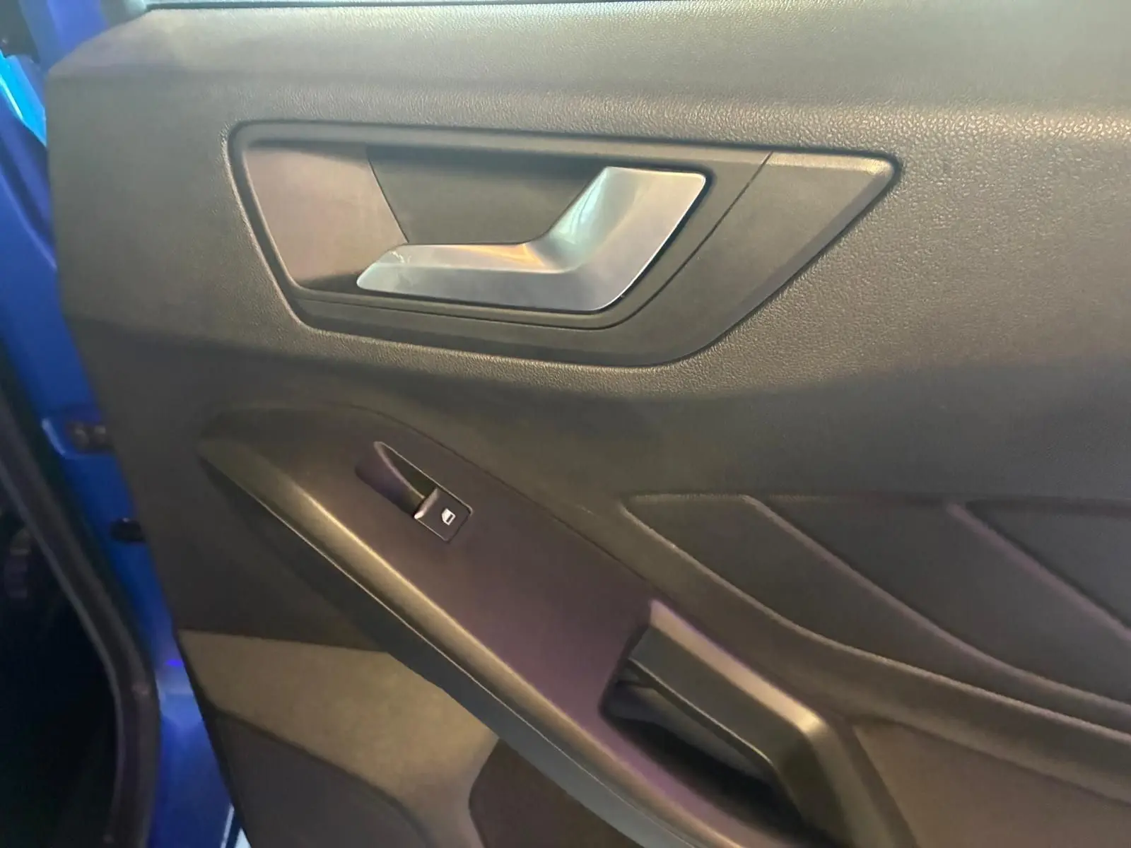 Détail de la porte intérieure côté gauche d’une Ford Focus 2024 bleue, avec poignée argentée et commande de vitre.