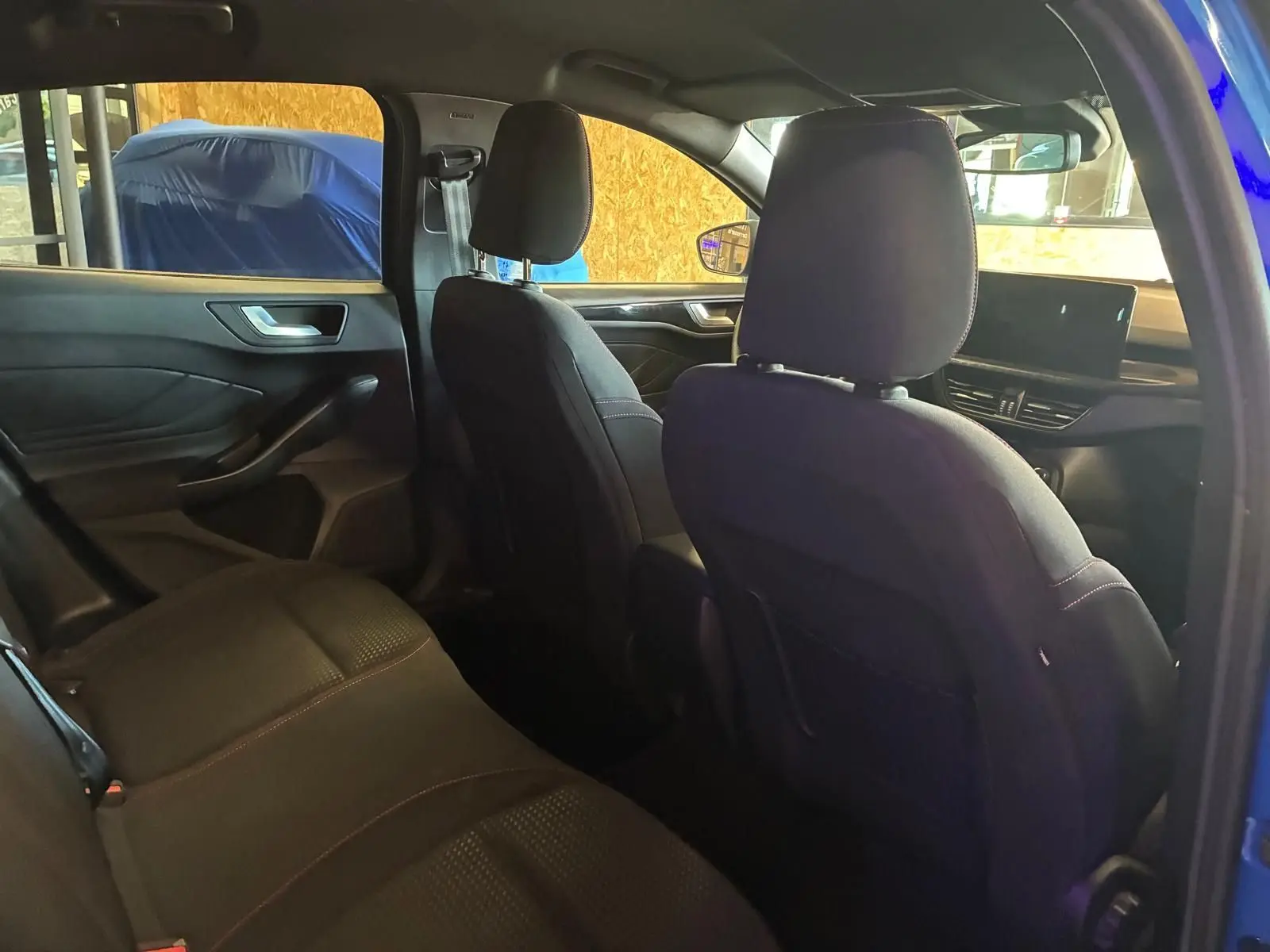 Vue intérieure arrière côté gauche de la Ford Focus 2024 bleu, sièges tissu noir avec surpiqûres rouges et tableau de bord visible.