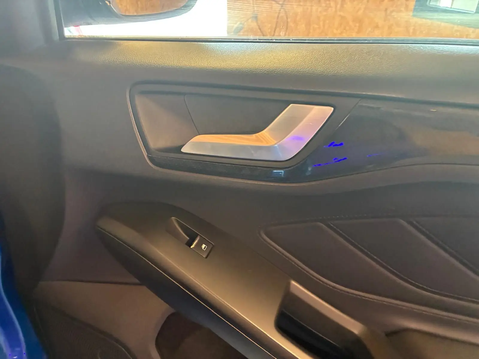 Détail de la porte intérieure côté gauche de la Ford Focus 2024 bleue, avec poignée argentée et commande de fenêtre.