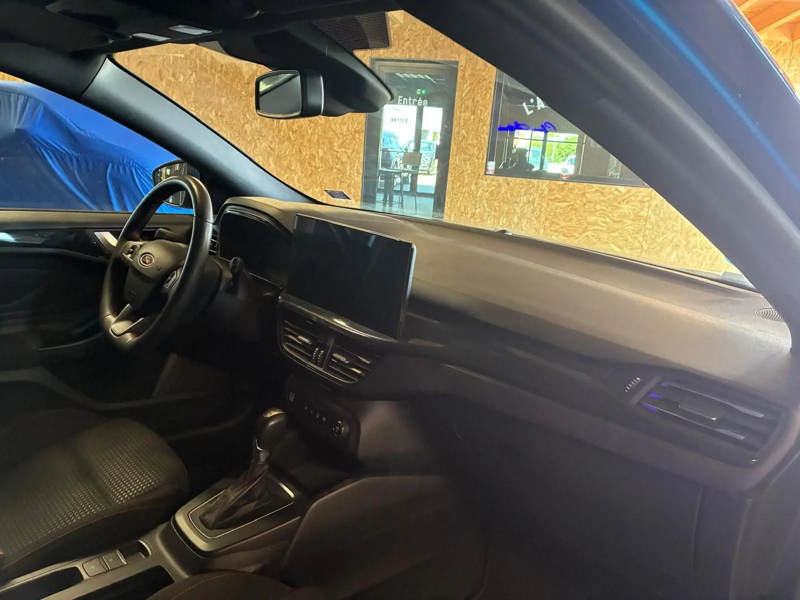 Vue intérieure côté conducteur de la Ford Focus bleu 2024, montrant le tableau de bord et la console centrale avec écran tactile.