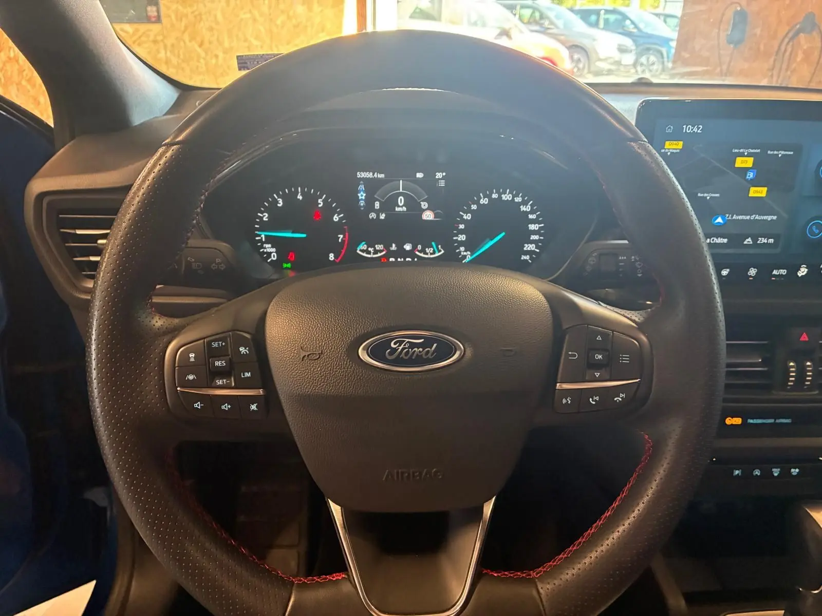 Vue centrée sur le volant noir avec surpiqûres rouges de la Ford Focus bleu 2024, tableau de bord et écran tactile visibles.