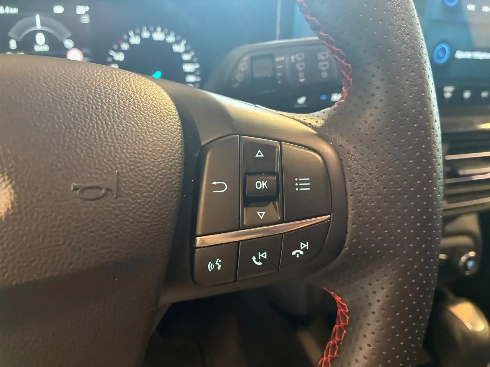 Gros plan sur les commandes au volant en cuir noir perforé avec surpiqûres rouges de la Ford Focus 2024.