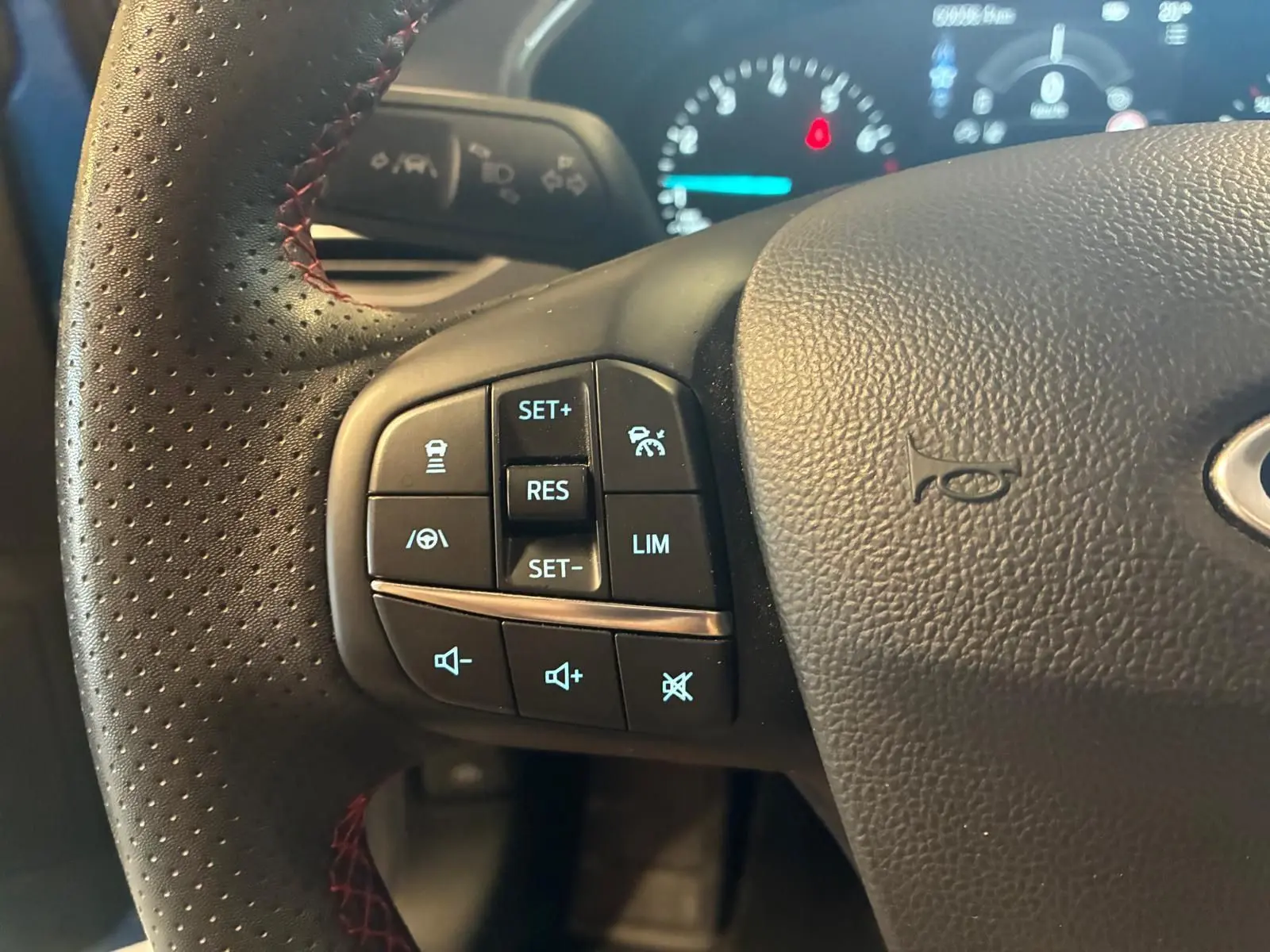 Gros plan sur le volant noir perforé de la Ford Focus 2024, avec commandes de régulateur et volume éclairées.