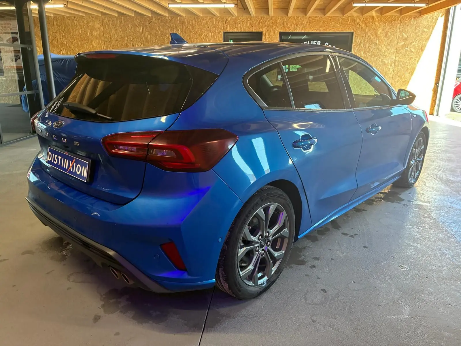 Ford Focus bleu vue 3/4 arrière droit en intérieur, avec jantes alliage et vitres teintées.