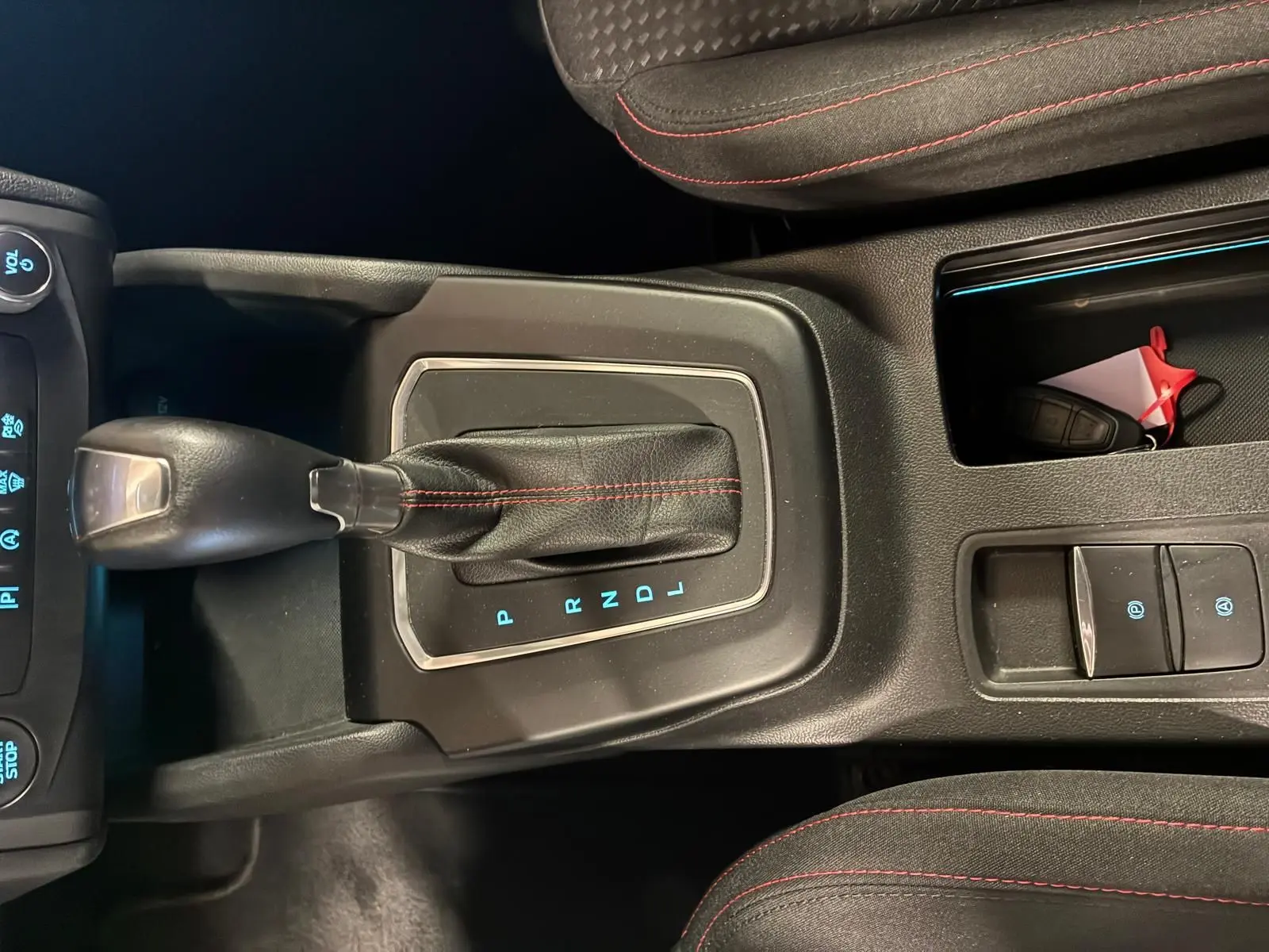 Vue intérieure centrée sur le levier de vitesses automatique noir avec surpiqûres rouges dans une Ford Focus bleue 2024.