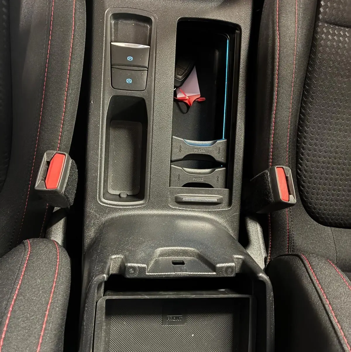 Vue plongeante sur la console centrale noire de la Ford Focus 2024, avec surpiqûres rouges et rangements ouverts.