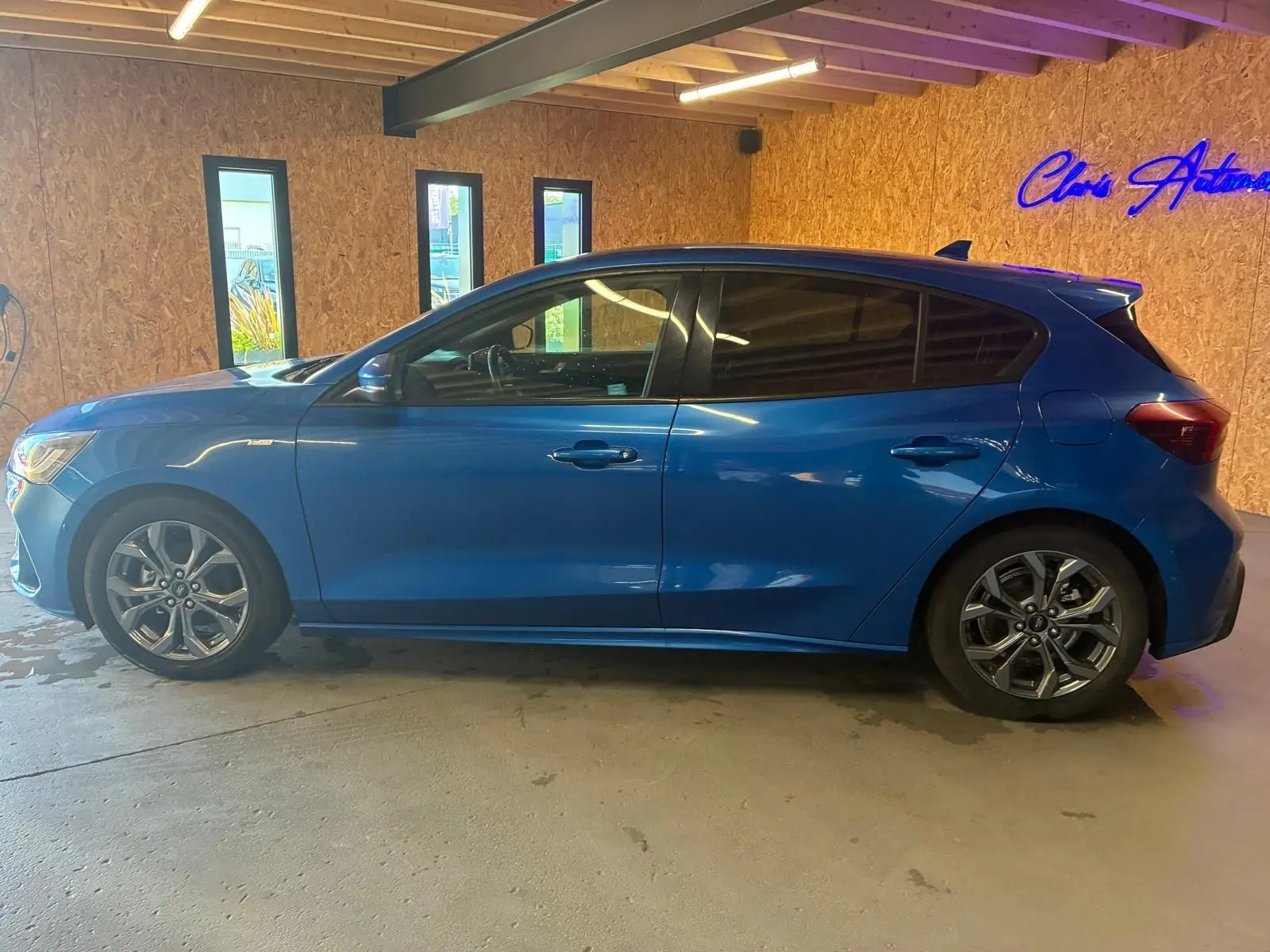 Vue de profil côté gauche d'une Ford Focus bleu 2024 ST Line avec jantes alliage et vitres teintées, stationnée en intérieur.