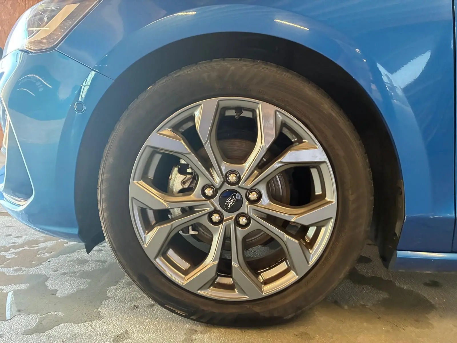 Gros plan sur la roue avant gauche d'une Ford Focus bleue 2024, mettant en valeur la jante alliage au design moderne.