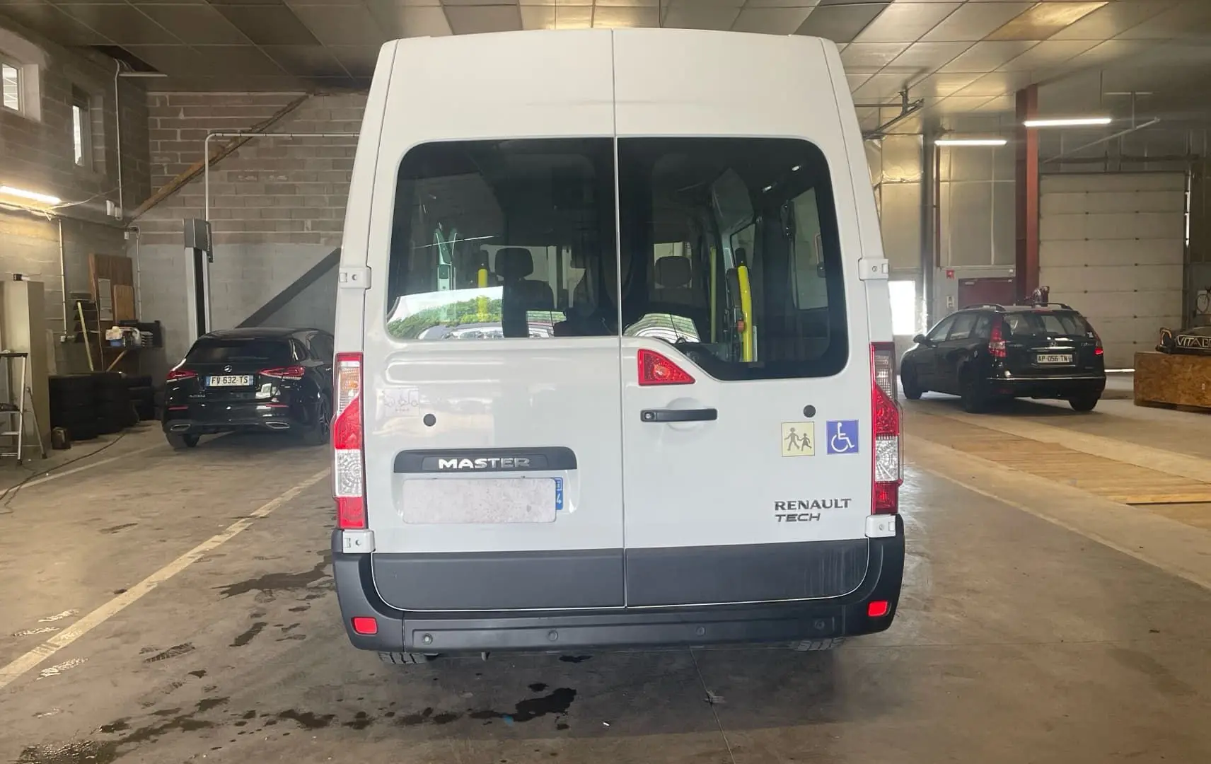 Vue arrière du Renault Master blanc TPMR avec rampe et stickers d’accessibilité, stationné en intérieur.