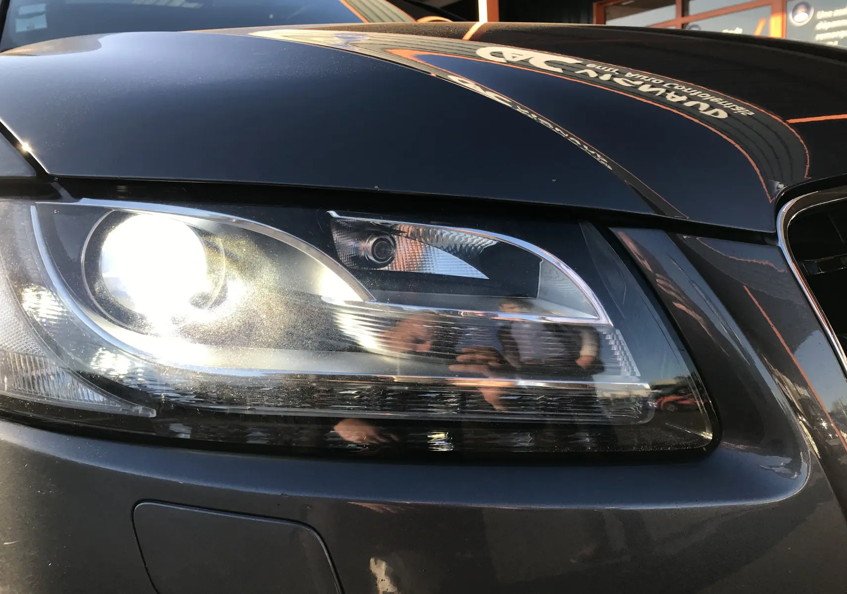 Gros plan sur le phare avant gauche d'une Audi A5 Coupé gris dauphin 2012 avec reflets sur la carrosserie.