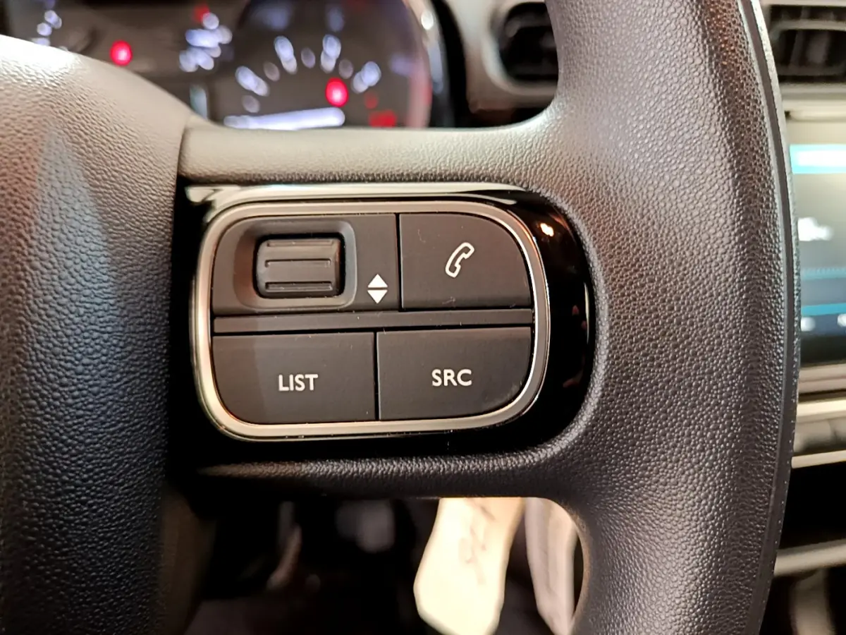 Gros plan sur les commandes gauche du volant noir d'une Citroën C3 PureTech 82 essence 2019, avec tableau de bord flou en arrière-plan.