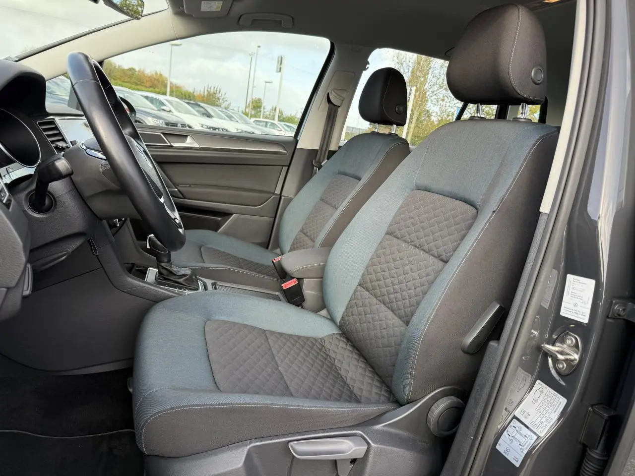 Vue intérieure côté conducteur de la Volkswagen Golf Sportsvan gris Urano, montrant les sièges avant en tissu bicolore.