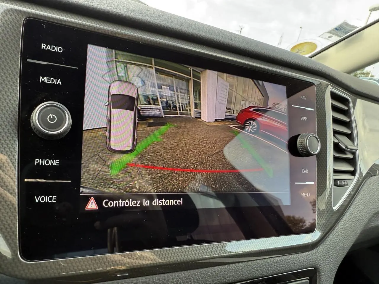 Écran de la caméra de recul dans une Volkswagen Golf Sportsvan gris Urano, affichant la zone arrière avec guidage de distance.