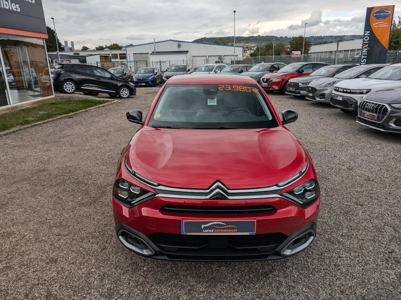 Vue avant d'une Citroën C4 rouge foncé 2024 avec calandre chromée et prix affiché sur pare-brise