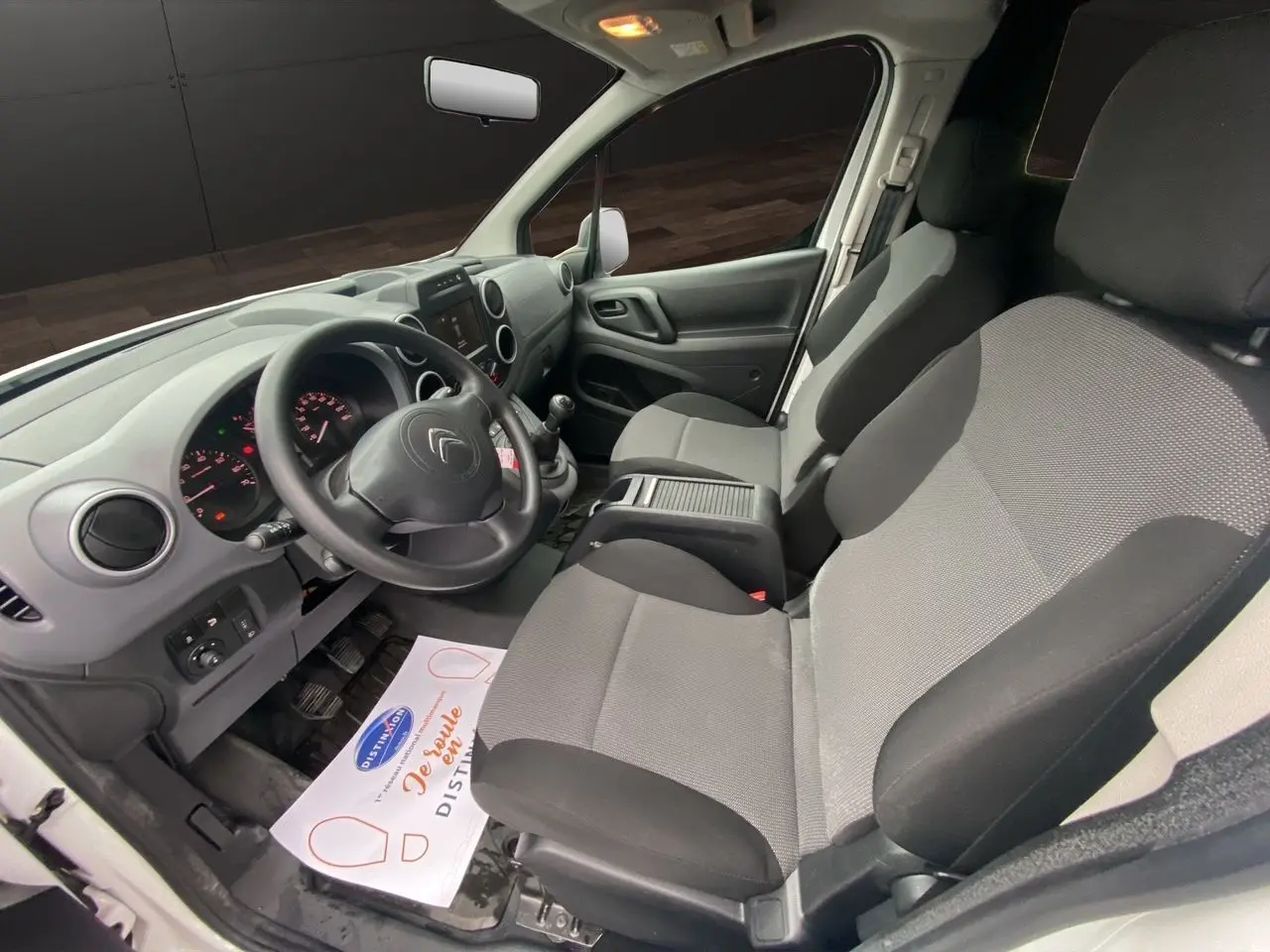 Vue intérieure côté conducteur du Citroën Berlingo blanc 2018, montrant le tableau de bord et les sièges avant gris et noirs.