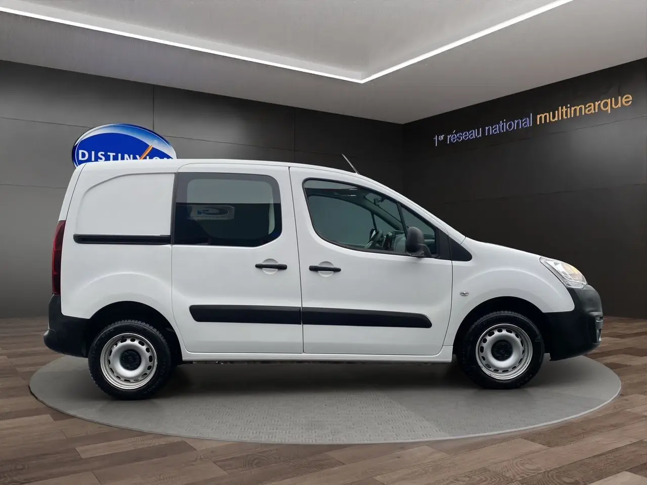 Vue de profil côté droit du Citroën Berlingo blanc 2018 version Van M BlueHDi avec protections noires sur fond intérieur showroom.