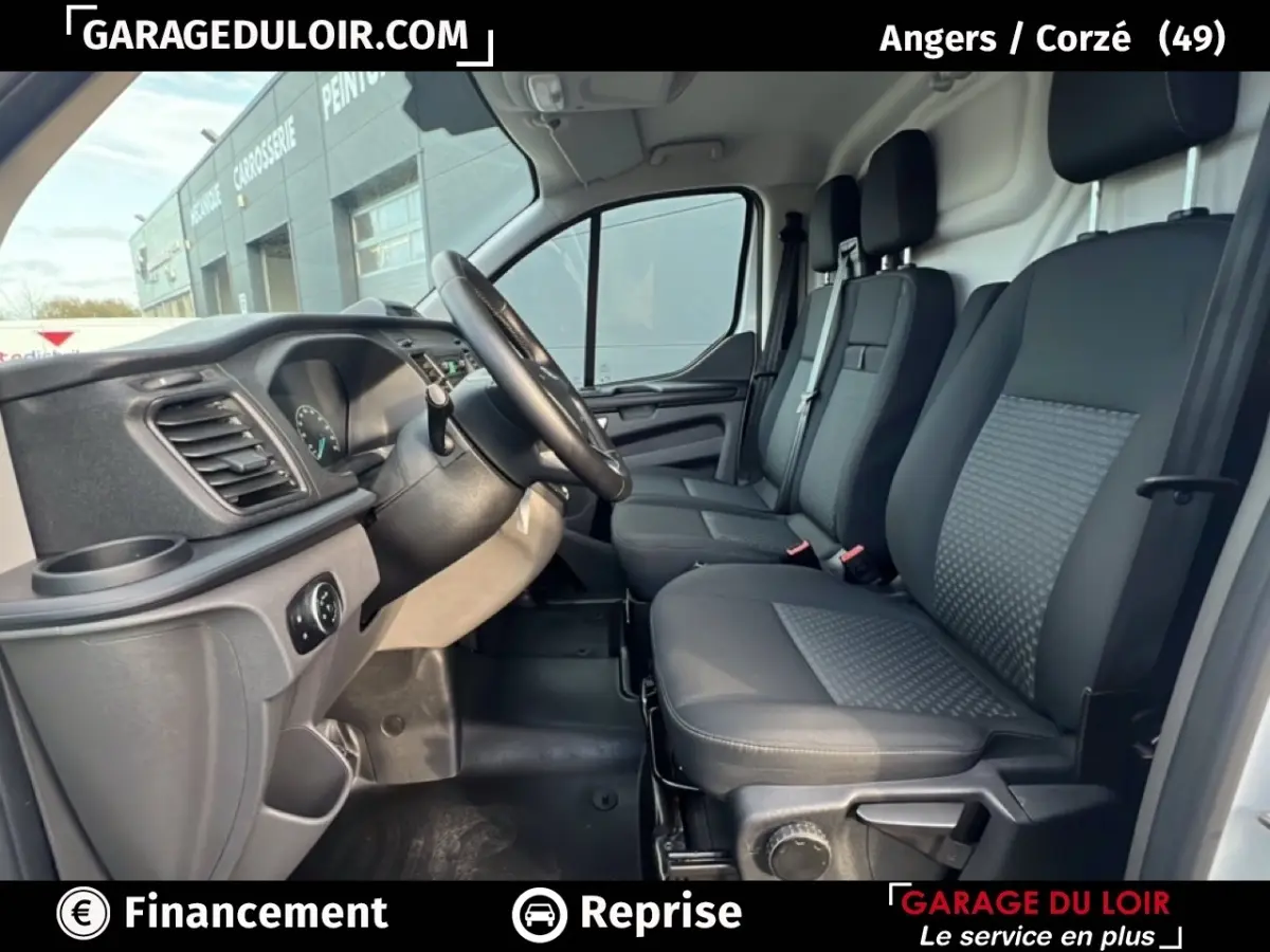 Intérieur du Ford Transit Custom blanc 2023, vue côté conducteur montrant sièges noirs et tableau de bord fonctionnel.