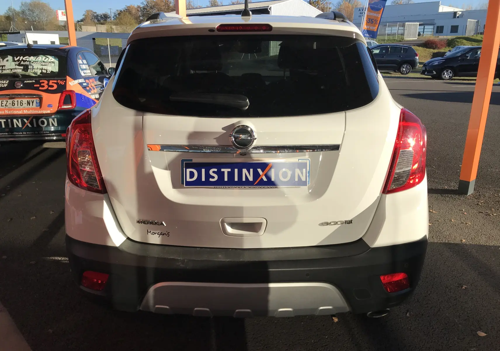 Vue arrière d'un Opel Mokka blanc 2015 avec logo et plaque Distinxion, feux rouges et lunette arrière teintée.