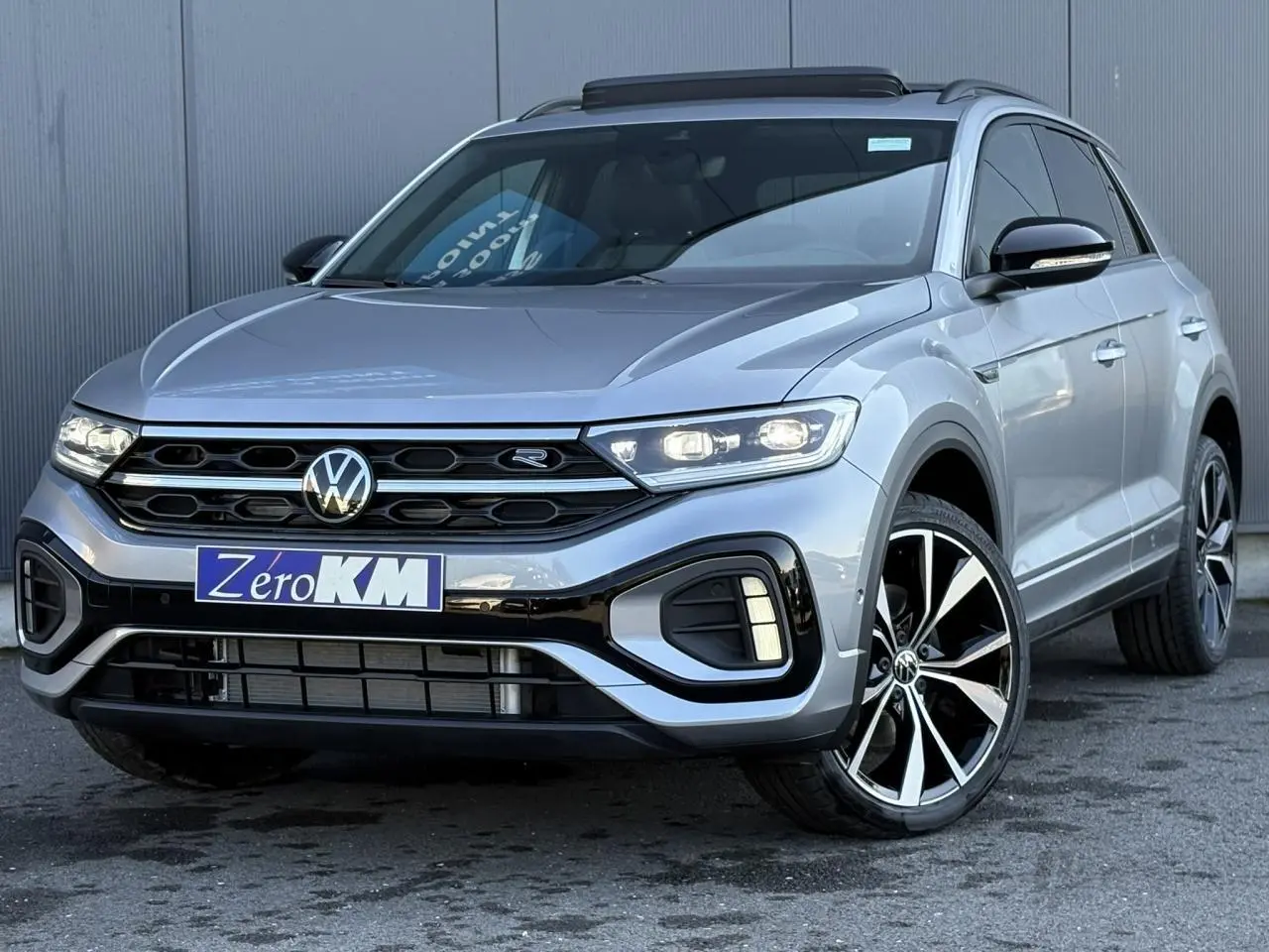 Volkswagen T-Roc gris pyrite en 3/4 avant droit avec jantes alliage 19 pouces et toit ouvrant visible.