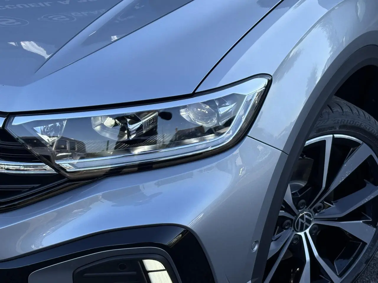 Gros plan sur l'avant droit du Volkswagen T-Roc gris pyrite, mettant en valeur le phare LED et la jante alliage 19 pouces.