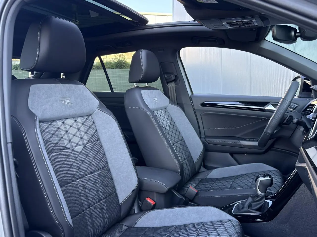 Vue intérieure côté conducteur du Volkswagen T-Roc R-Line 2025, sièges bicolores gris et noir avec logo R brodé.