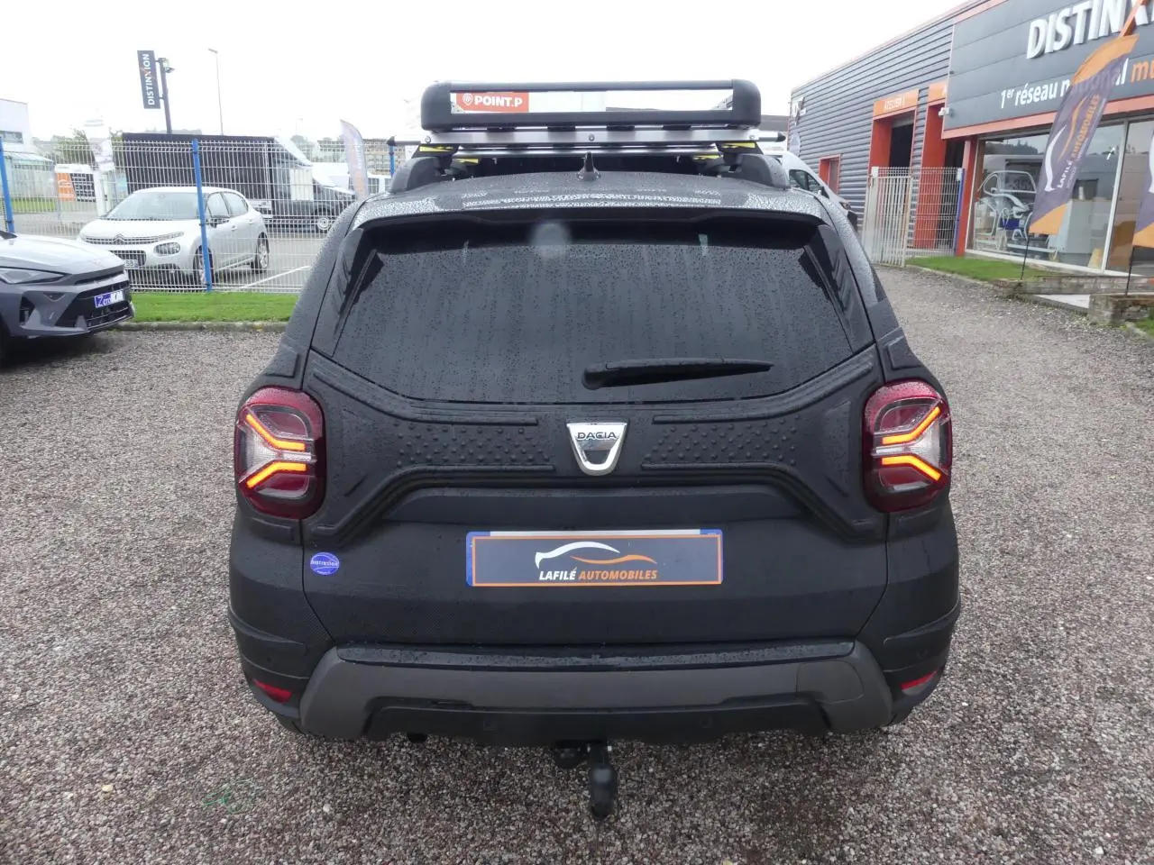 Vue arrière d'un Dacia Duster noir 2023 avec attelage fixe et galerie de toit, vitres arrière surteintées.