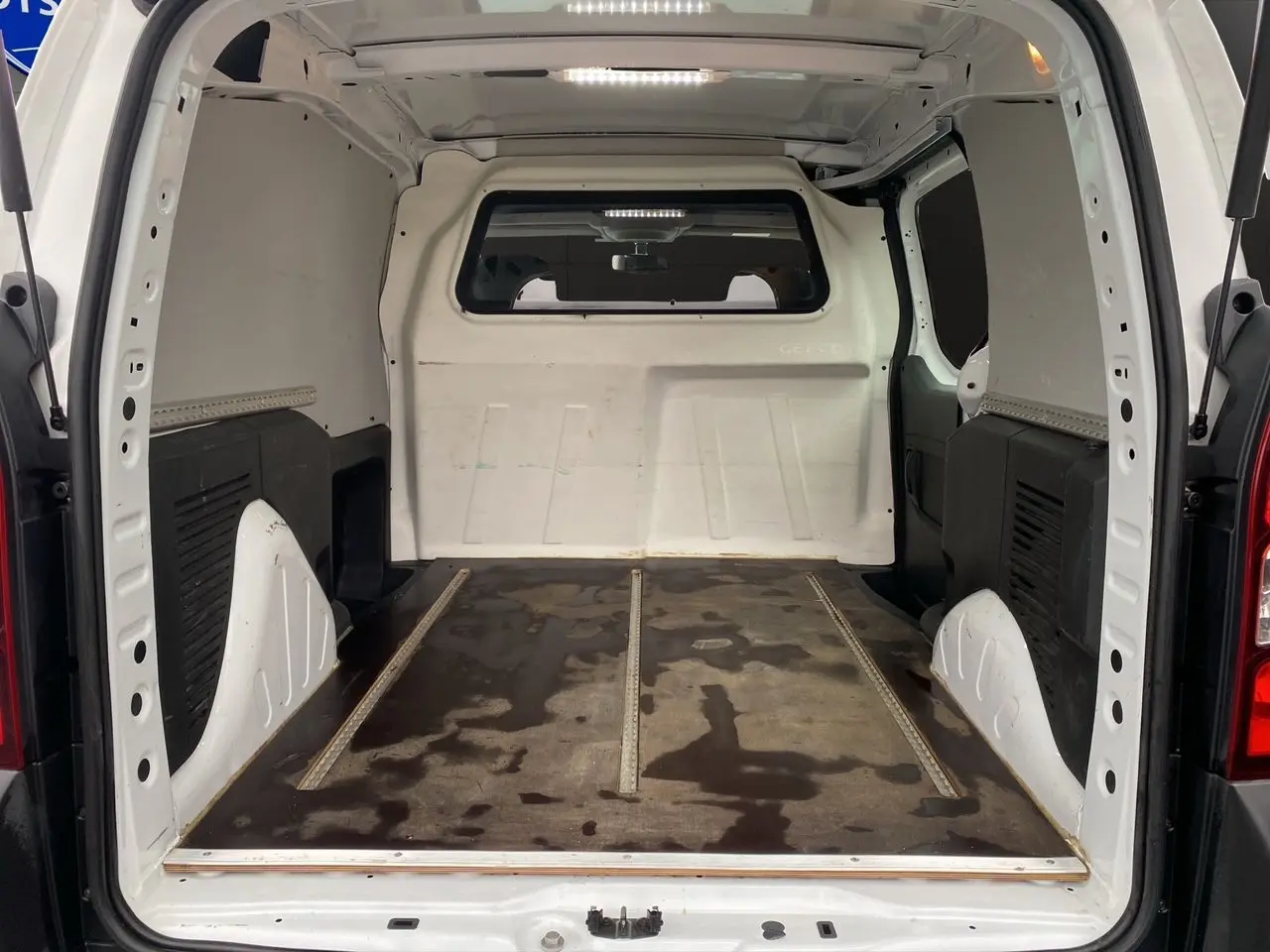 Vue intérieure arrière du Citroën Berlingo blanc 2018, montrant l’espace de chargement vide avec sol usé et parois blanches.