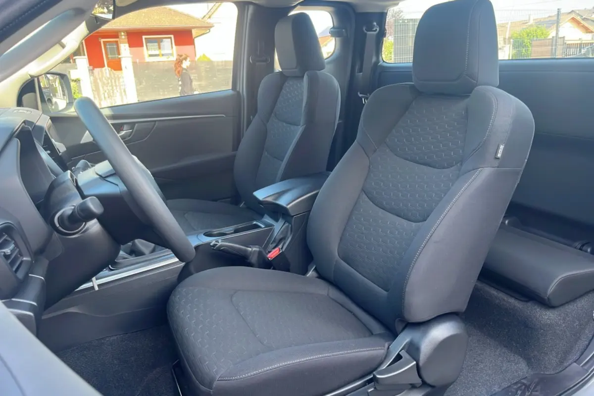 Vue intérieure côté gauche du pick-up Isuzu D-MAX 2026, sièges tissu gris foncé avec accoudoir central avant.